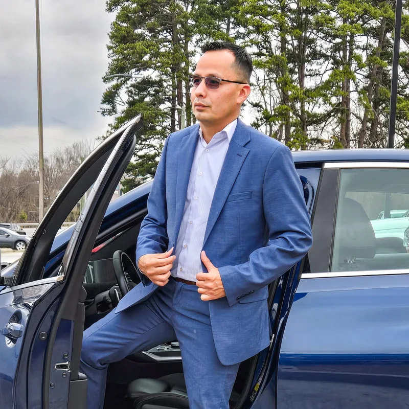 Daniel Rios con traje azul junto a un automóvil, fotografía de su perfil de Facebook